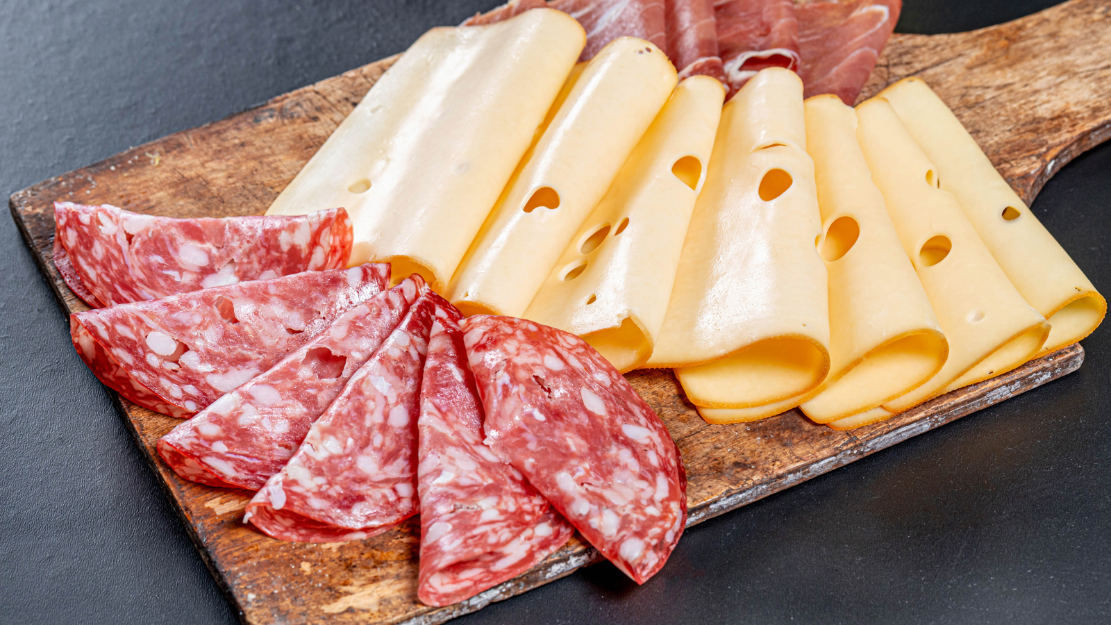 Колбаса, мясо и сыр нарезанный на разделочной доске 