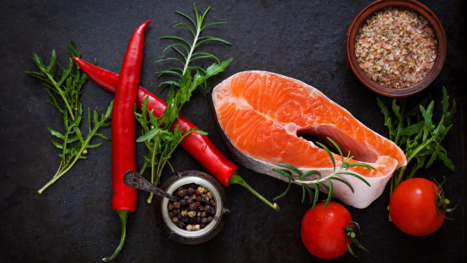 Кусок свежей красной рыбы на столе со специями, красным перцем и помидорами