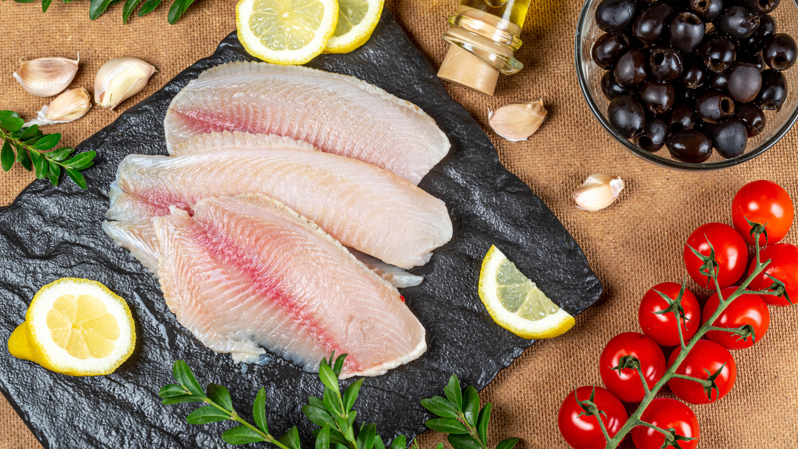 Филе рыбы на столе с лимоном, помидорами и оливками