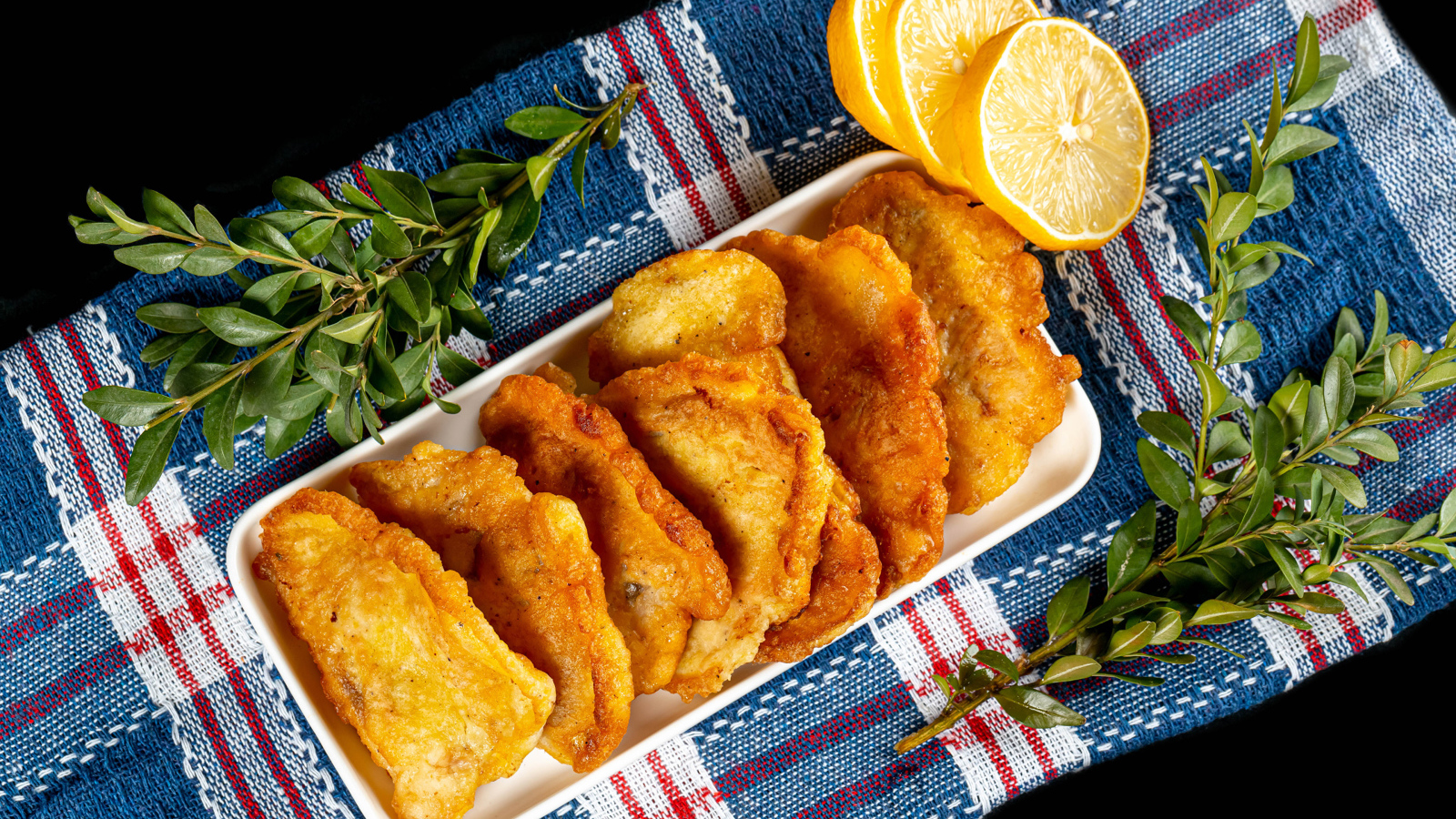 Жареная рыба в кляре на столе с лимоном и зеленью