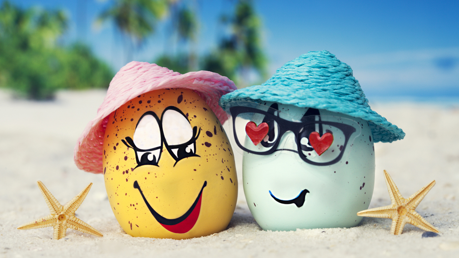 Два яйца в шляпах на песке с морскими звездами летом