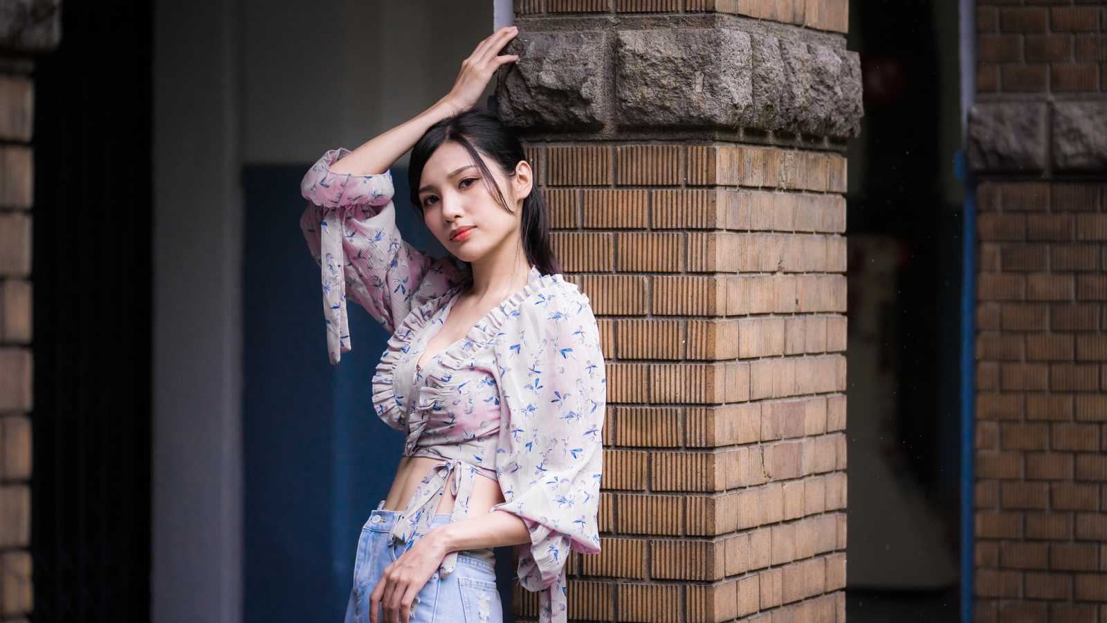 Красивая девушка азиатка стоит у кирпичной колонны 