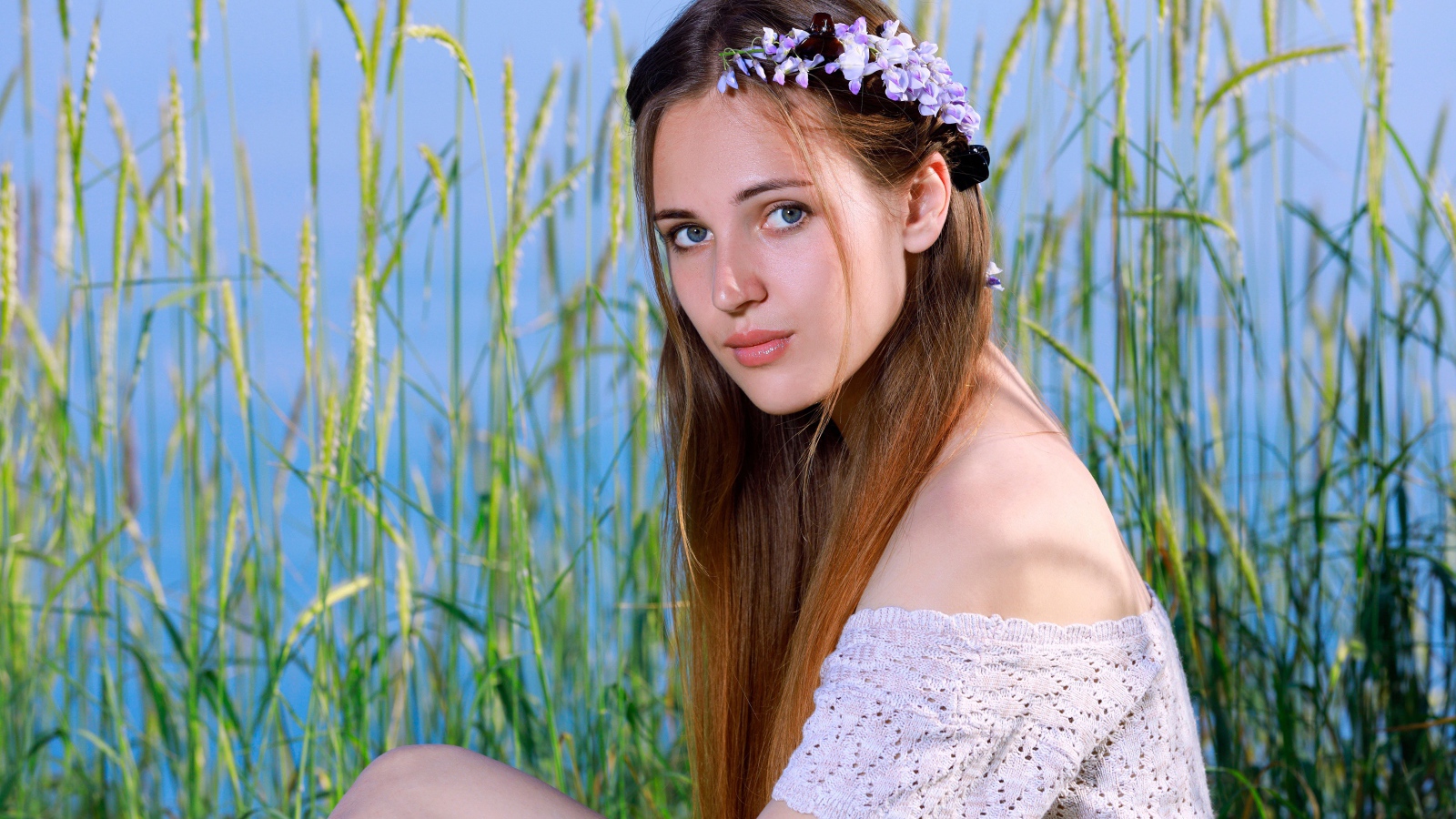 Красивая молодая девушка с венком на голове сидит на поле с колосьями 