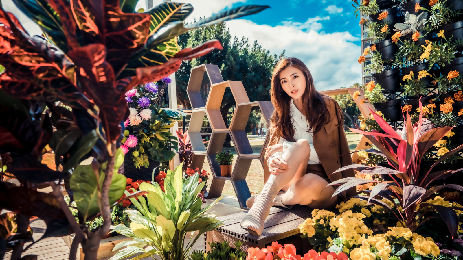 Молодая азиатка сидит возле клумбы с цветами