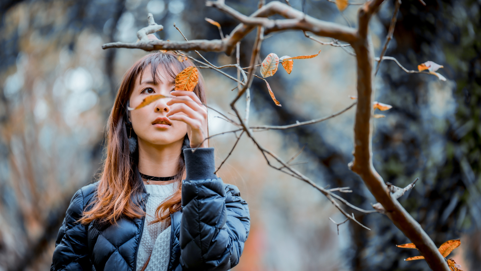 Девушка азиатка в черной куртке у дерева