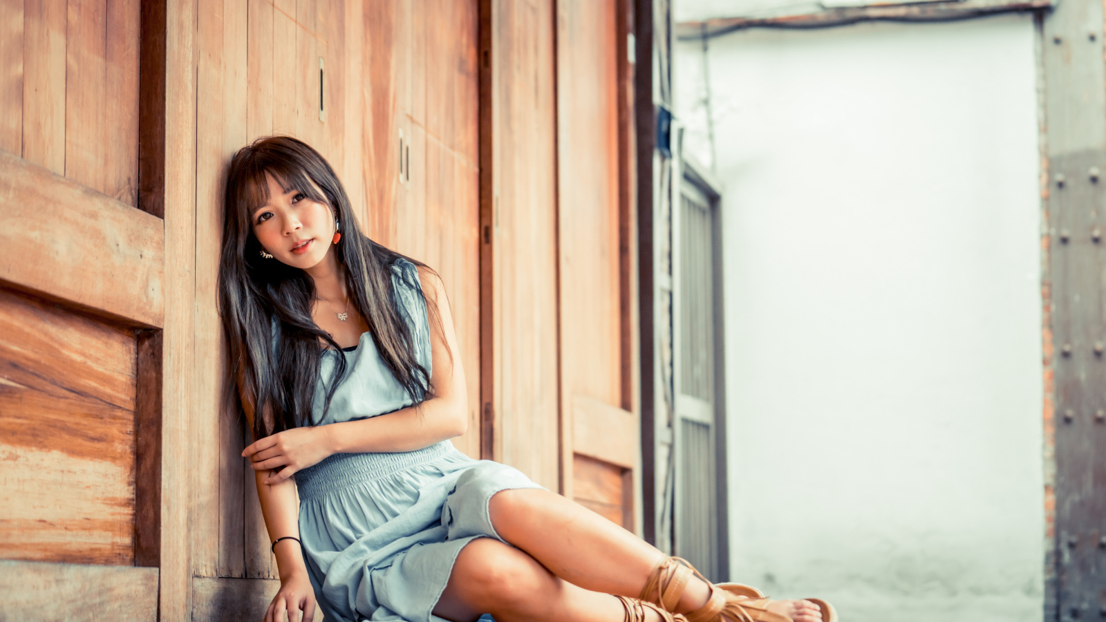 Девушка азиатка в платье сидит на полу у стены 