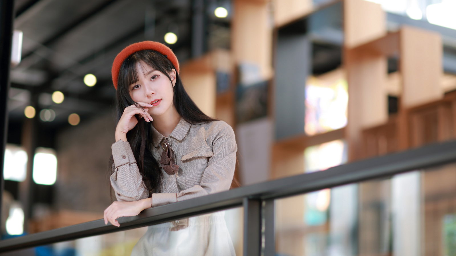 Азиатка в сером платье стоит у перил 