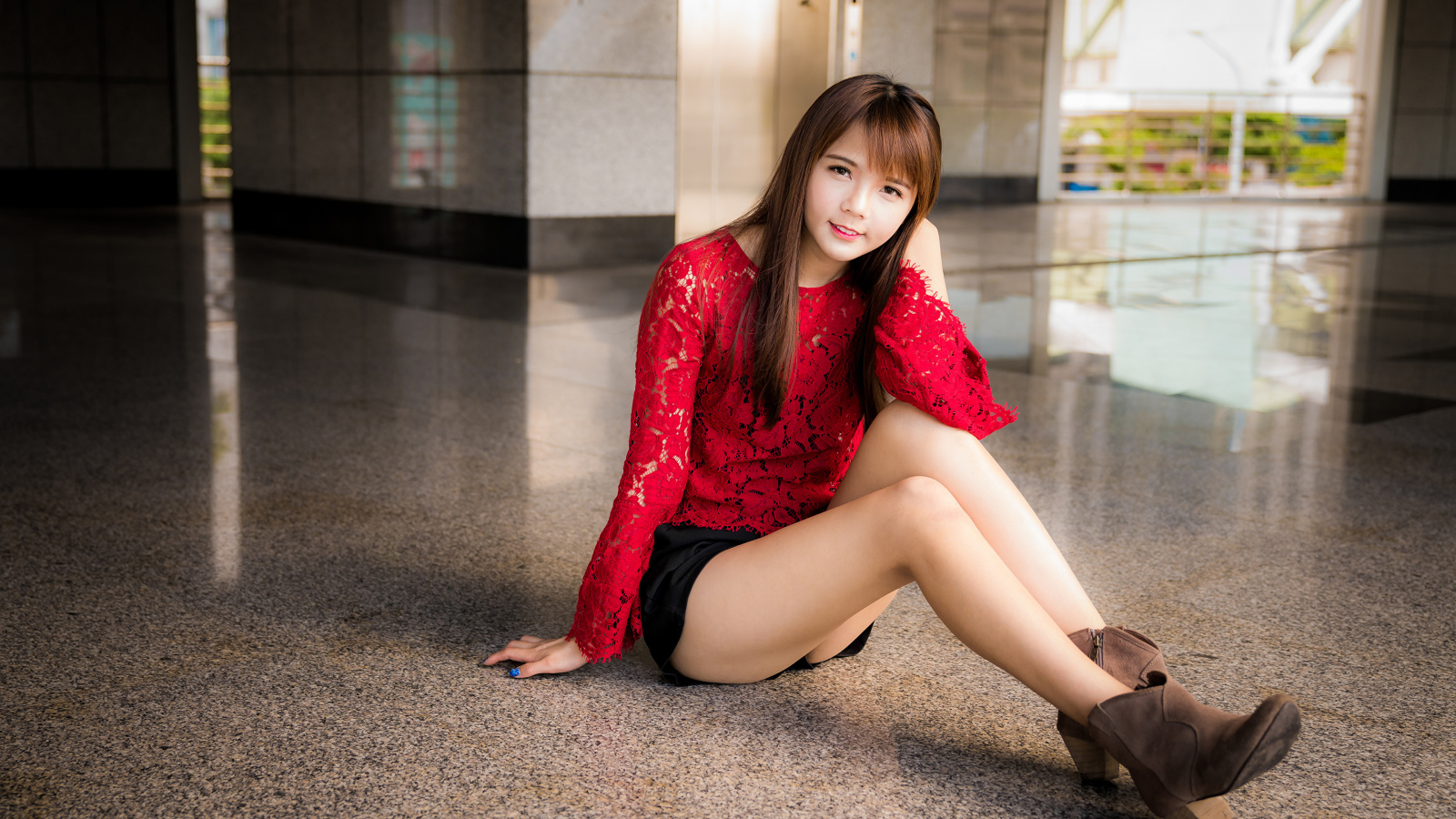 Красивая девушка азиатка в красной блузке сидит на полу