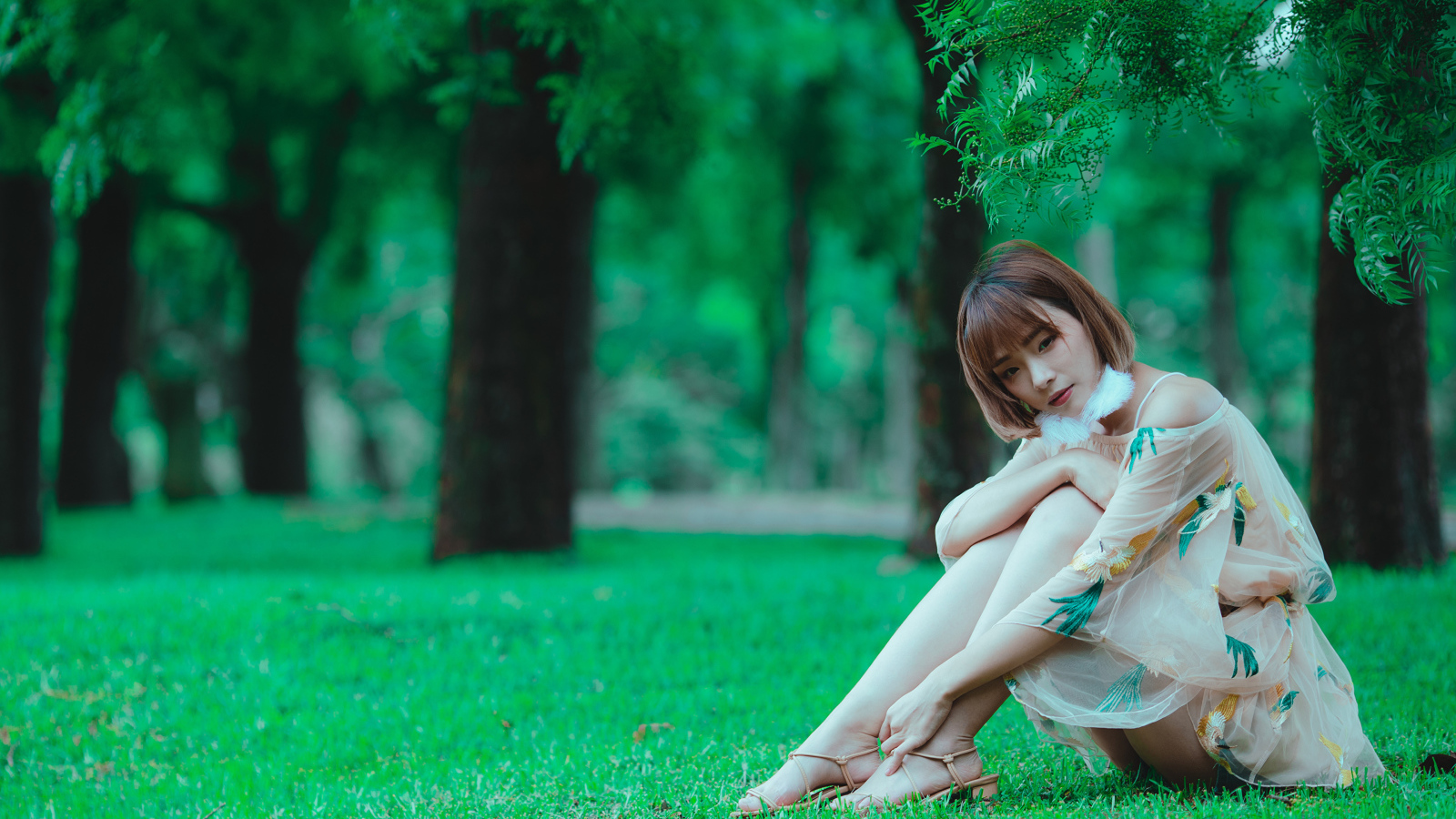 Красивая девушка азиатка сидит на зеленой траве в парке 