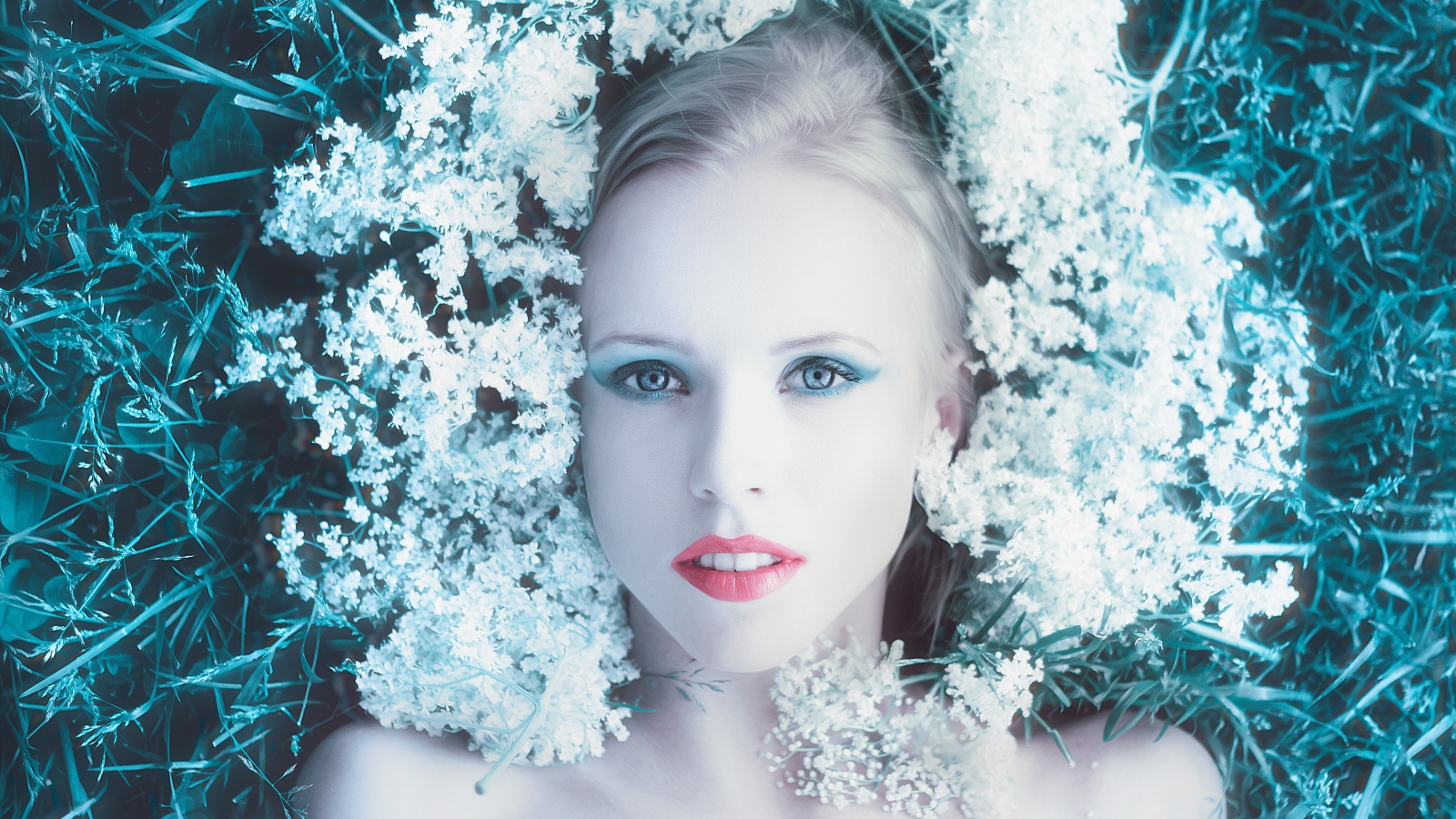 Красивая голубоглазая девушка на траве с белыми цветами