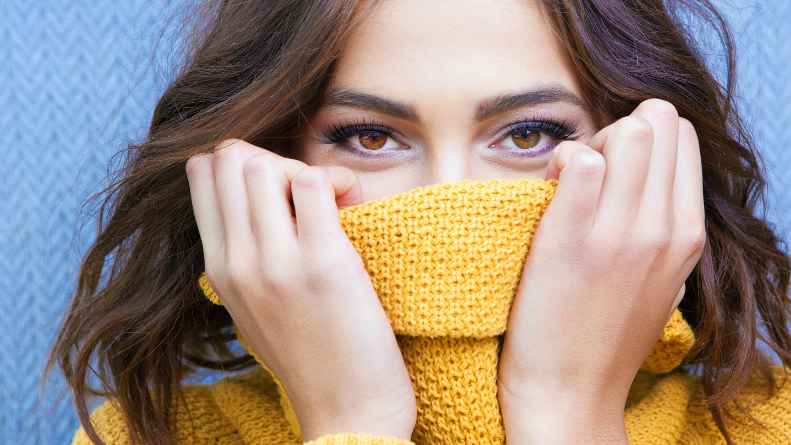 Красивая кареглазая девушка закрывает лицо свитером