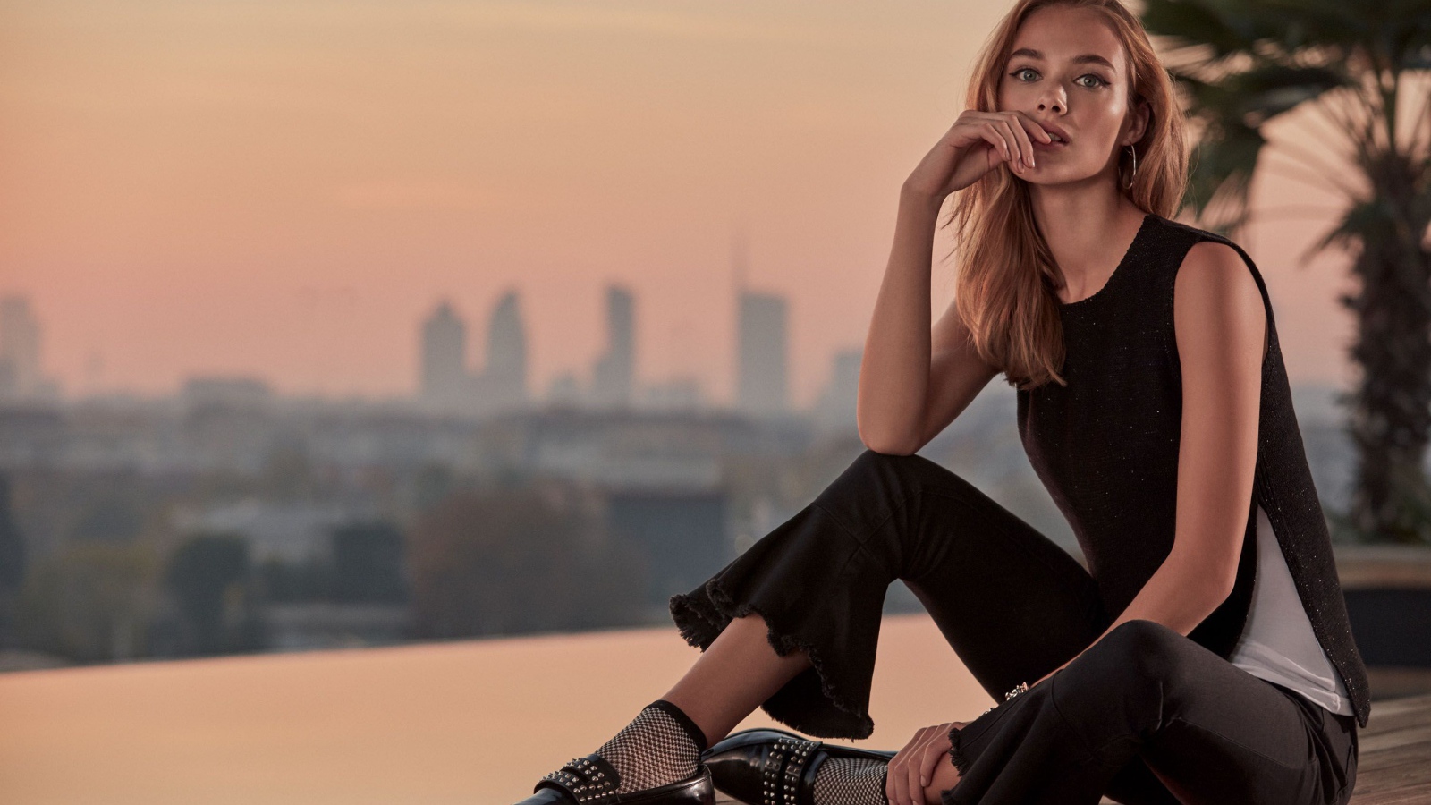 Красивая девушка в черном сидит  на мосту 