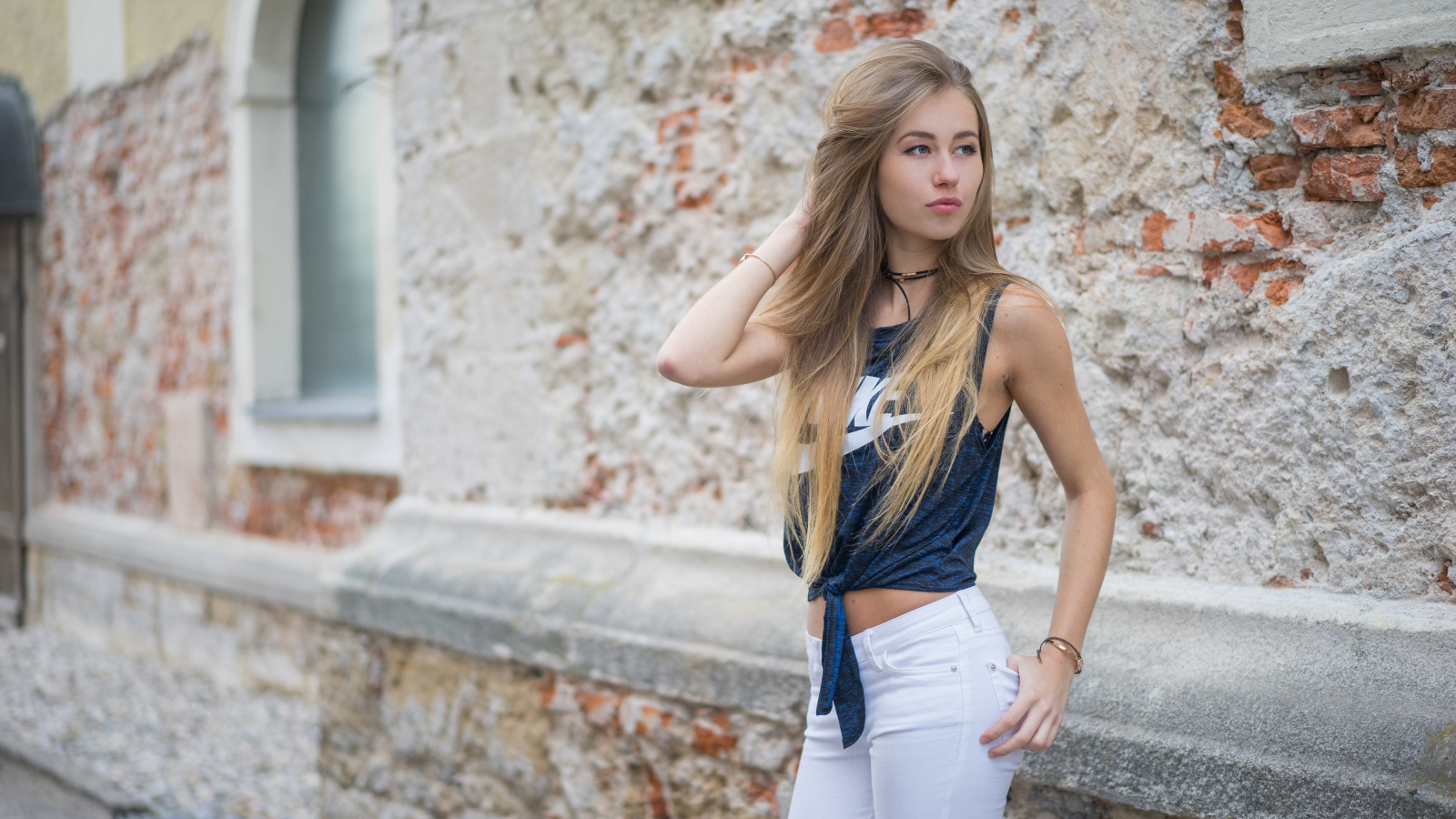 Красивая девушка в белых брюках стоит у стены 