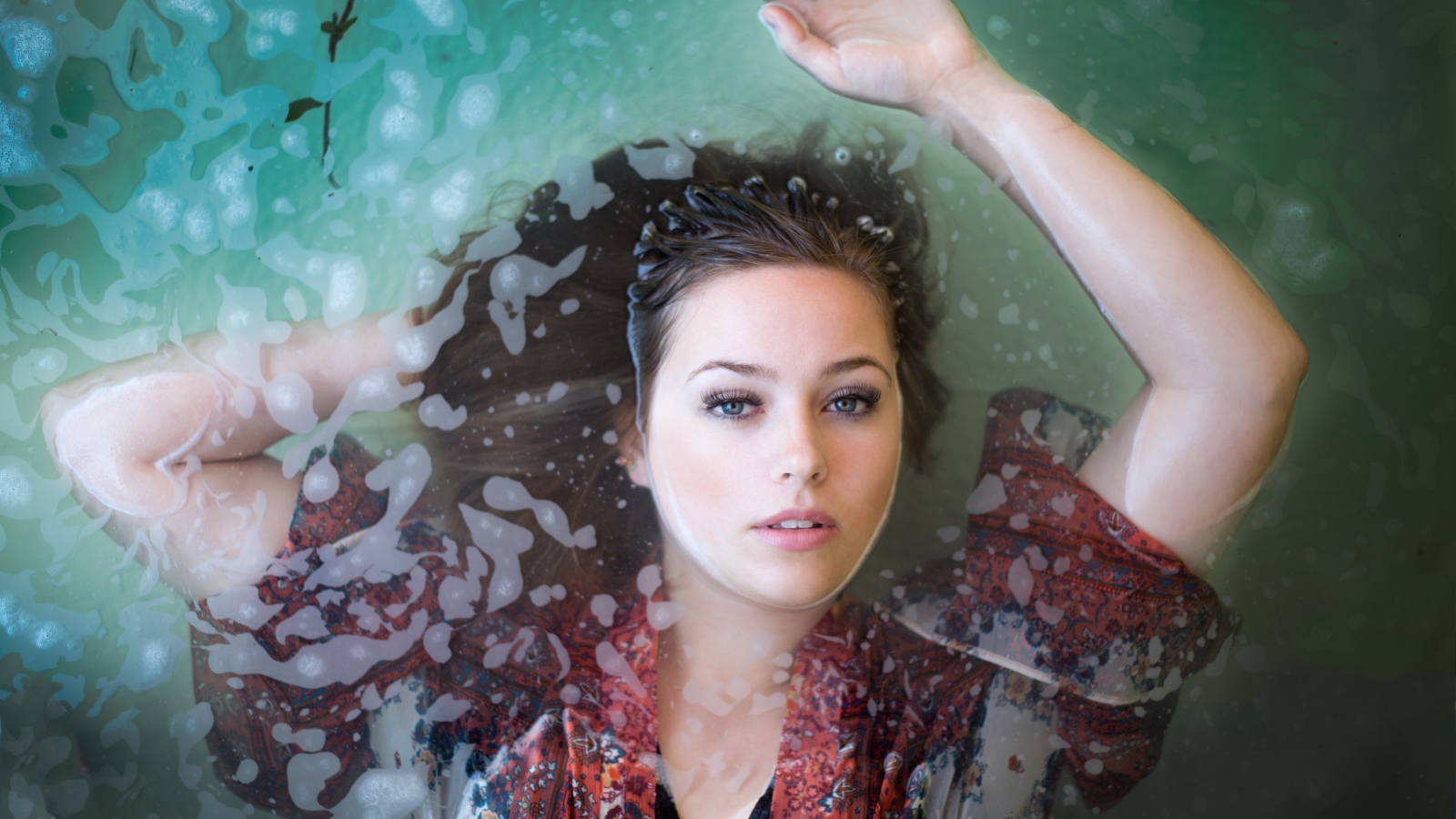 Красивая девушка лежит в одежде в воде 