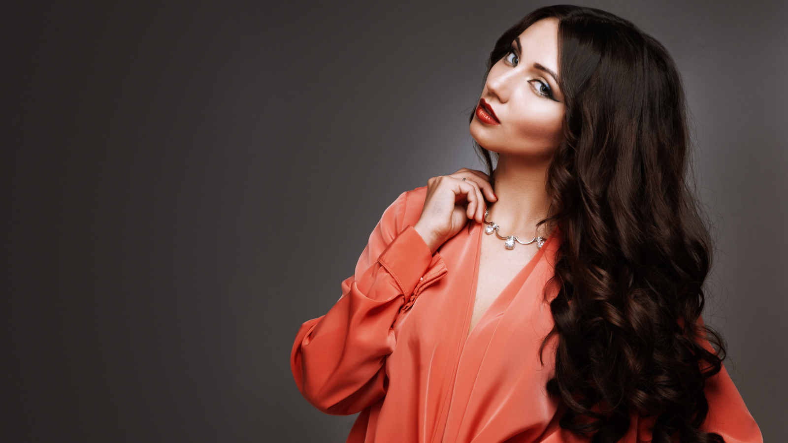 Красивая длинноволосая девушка в красной рубашке на сером фоне 