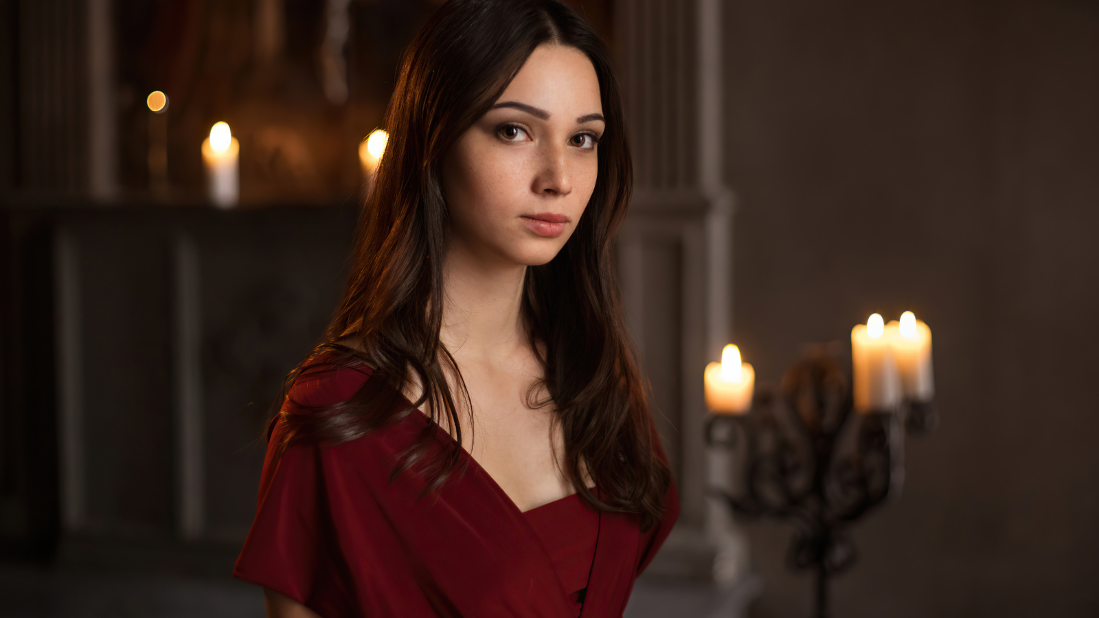 Кареглазая девушка в красном платье в комнате со свечами