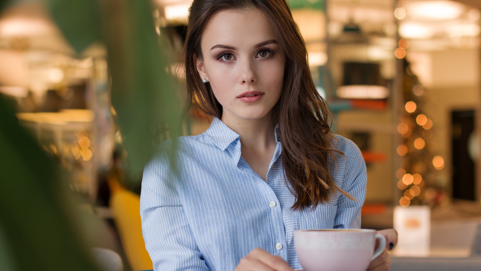 Girl in a blue shirt with a cup of coffee on a table in a cafe