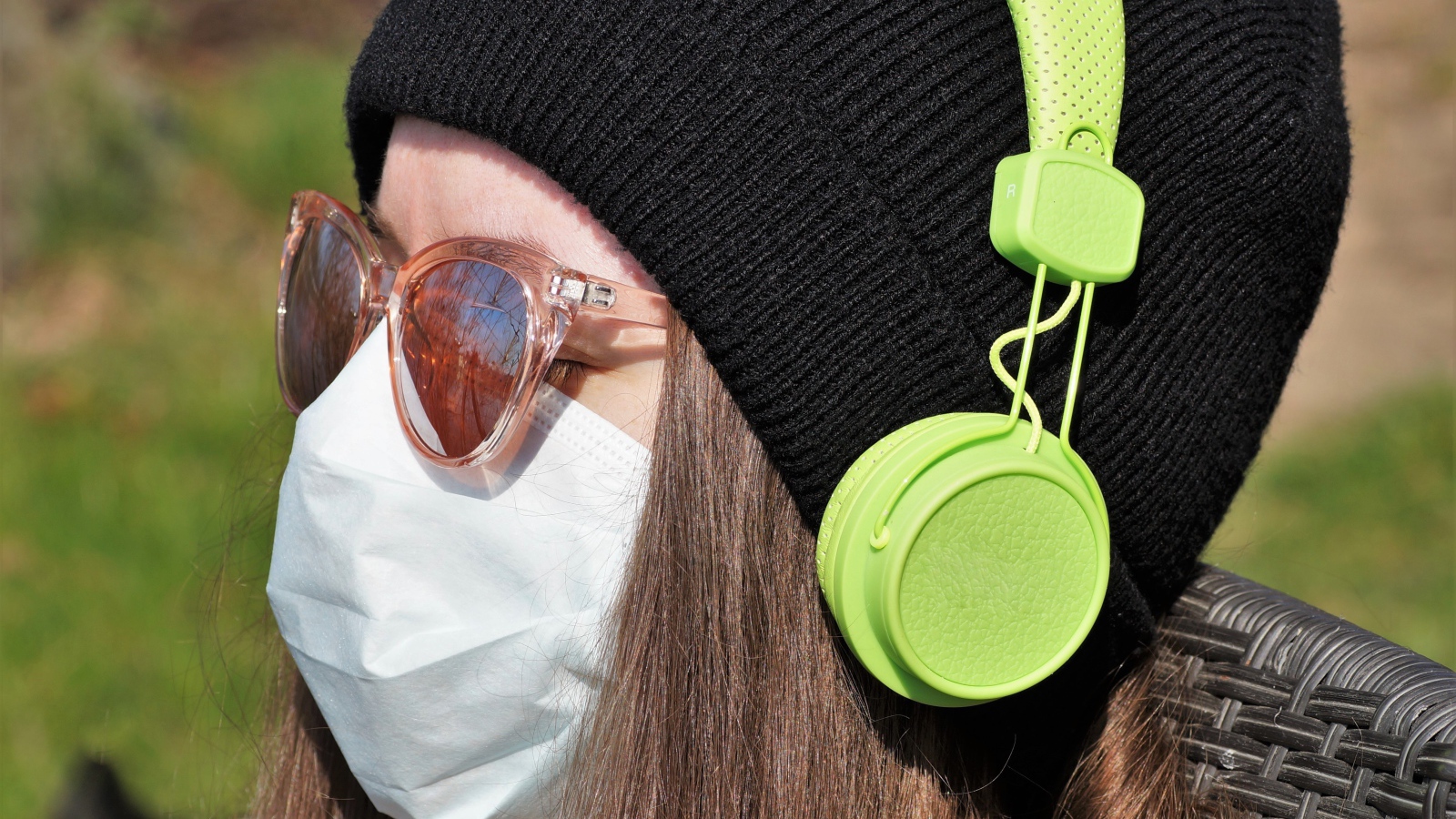 Девушка в медицинской маске на лице, в черной маске и наушниках