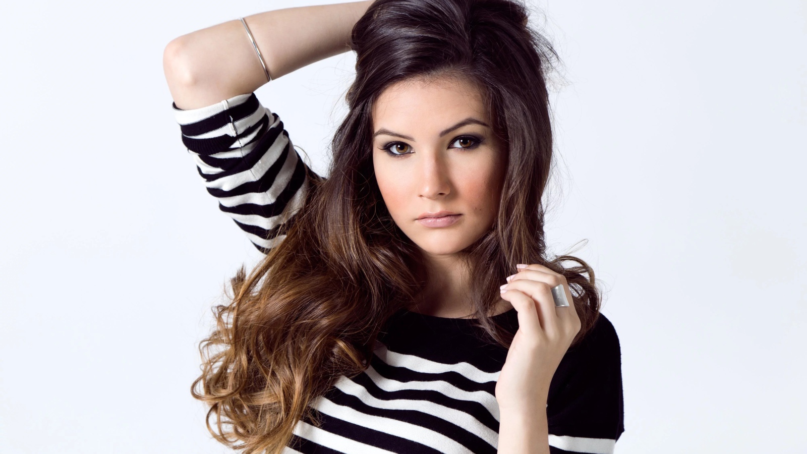 Девушка в полосатом свитере с рукой в волосах на белом фоне