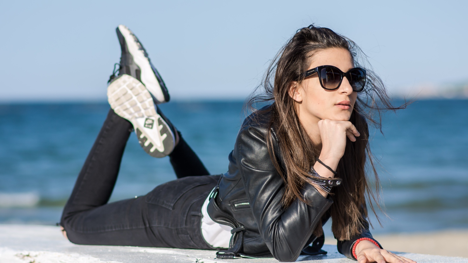 Девушка в черных очках и кожаной куртке на фоне моря