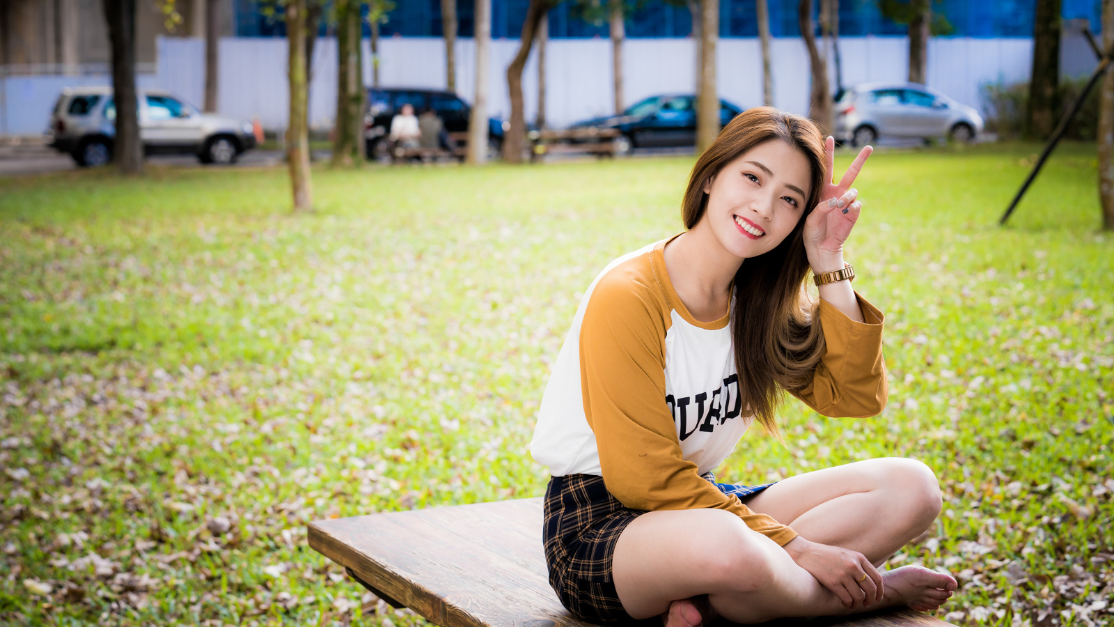 Улыбающаяся девушка азиатка сидит на лавке в парке 