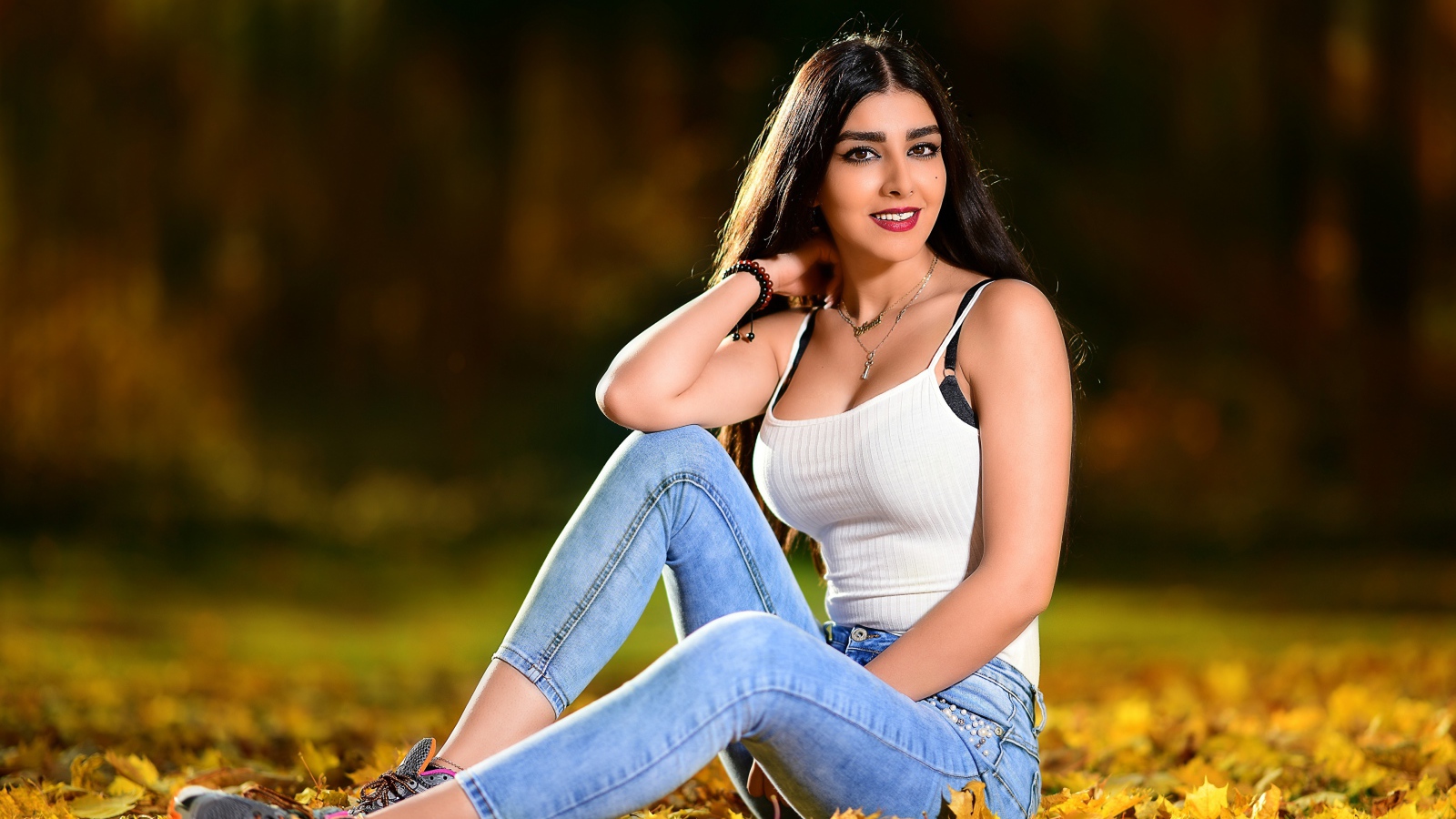 Улыбающаяся брюнетка сидит на опавшей листве