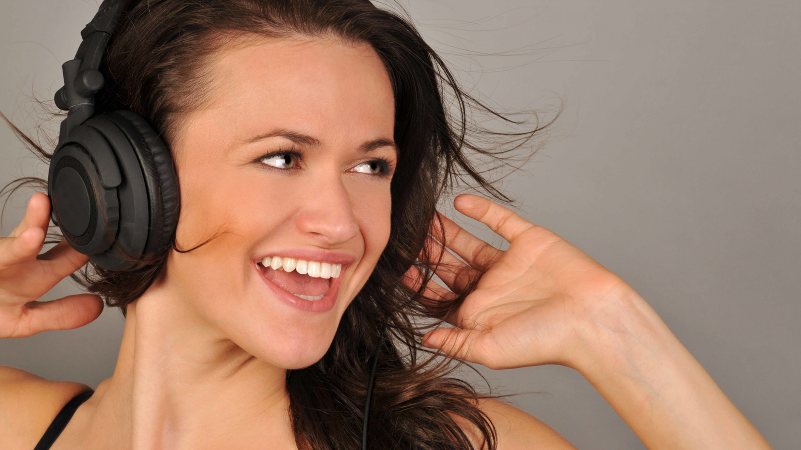 Улыбающаяся девушка в наушниках на сером фоне 