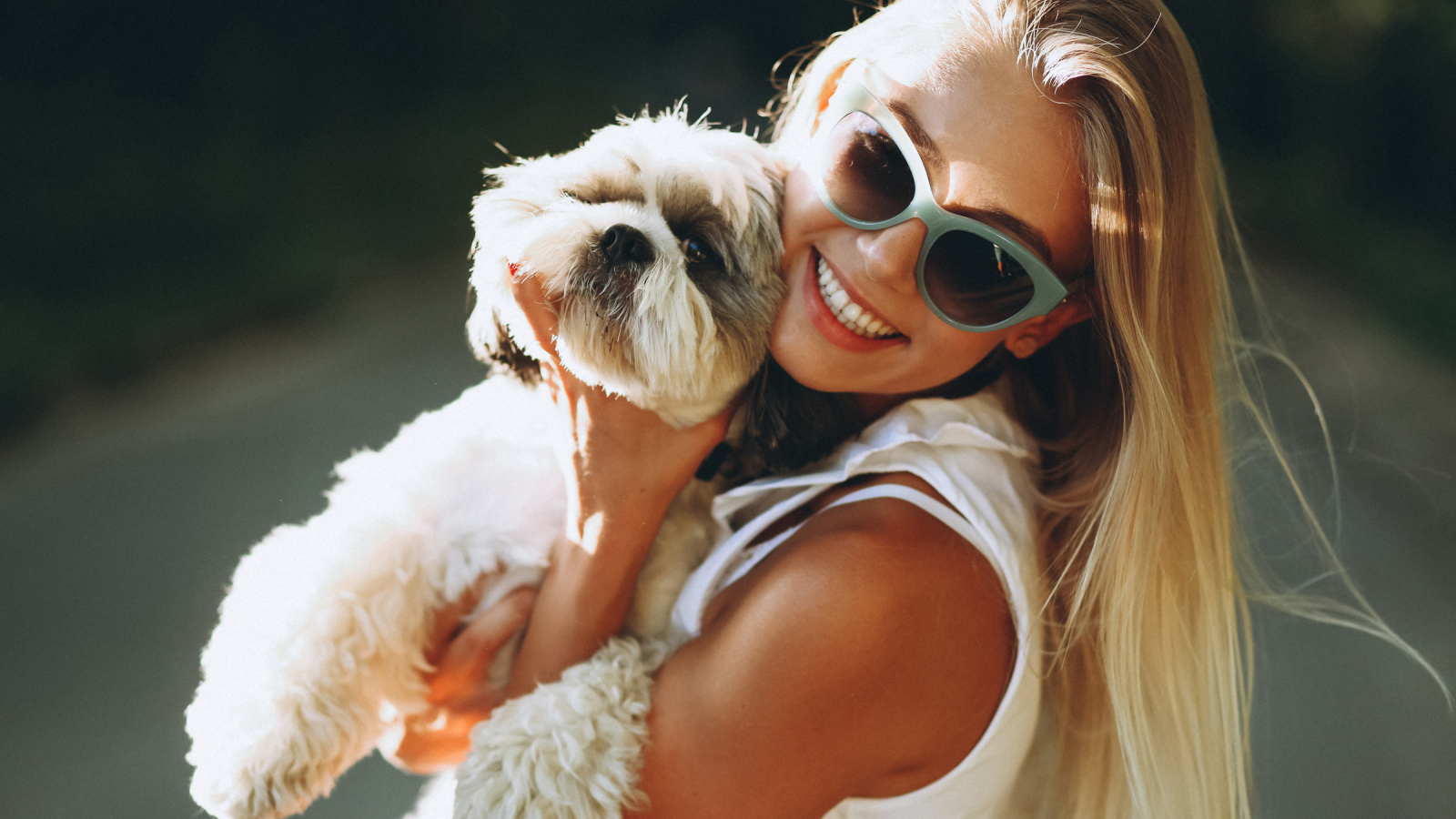 Улыбающаяся девушка в солнечных очках с собакой на руках
