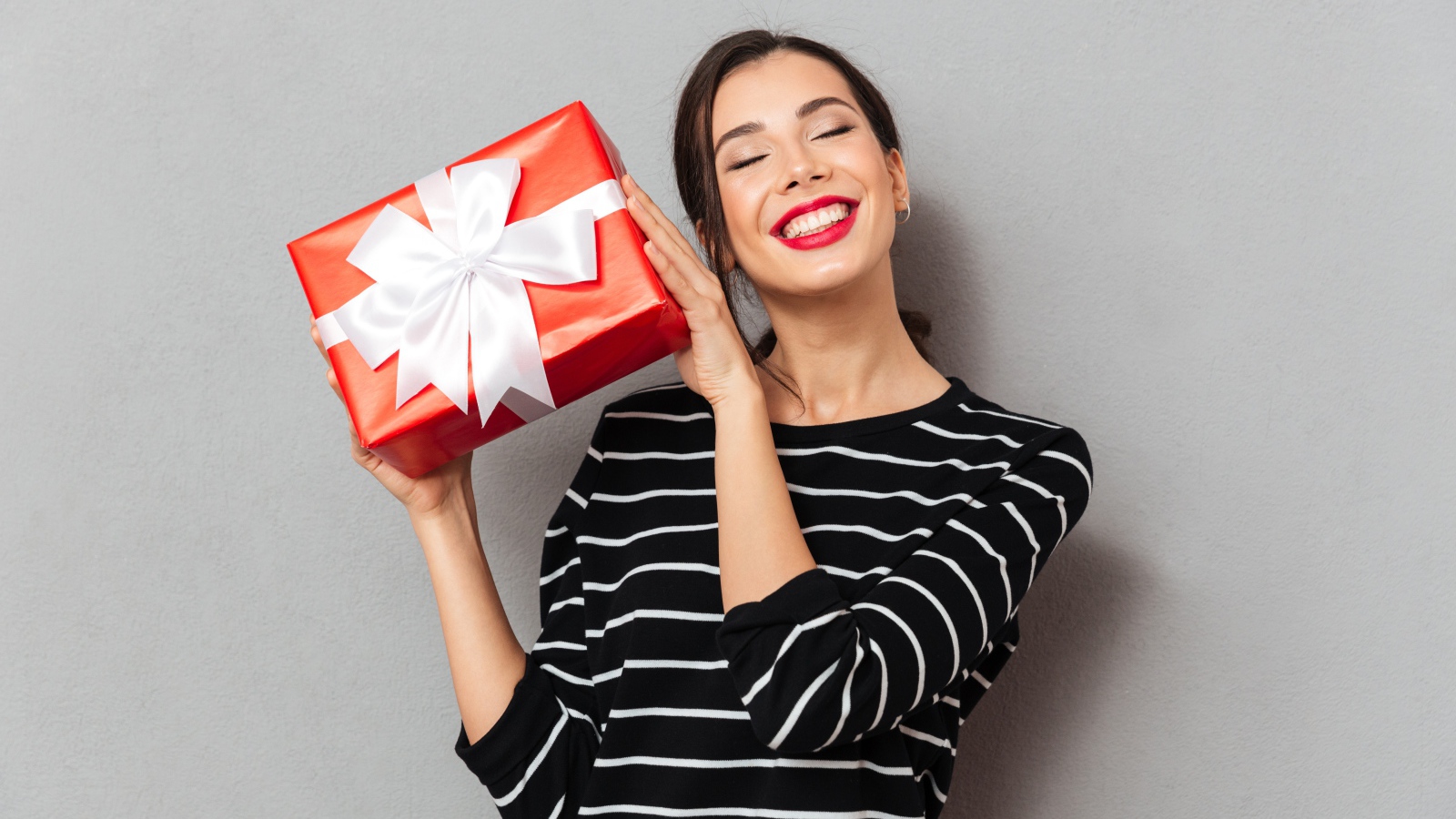 Улыбающаяся девушка с подарком в руках на сером фоне 