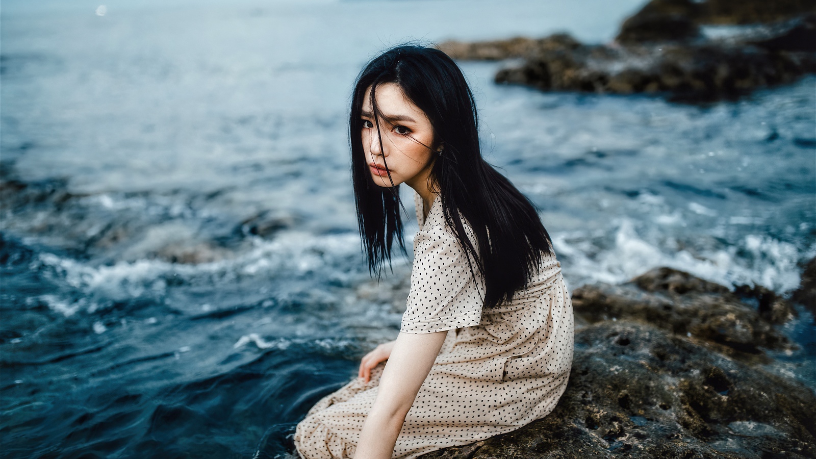 Young Asian girl sitting on a stone by the water