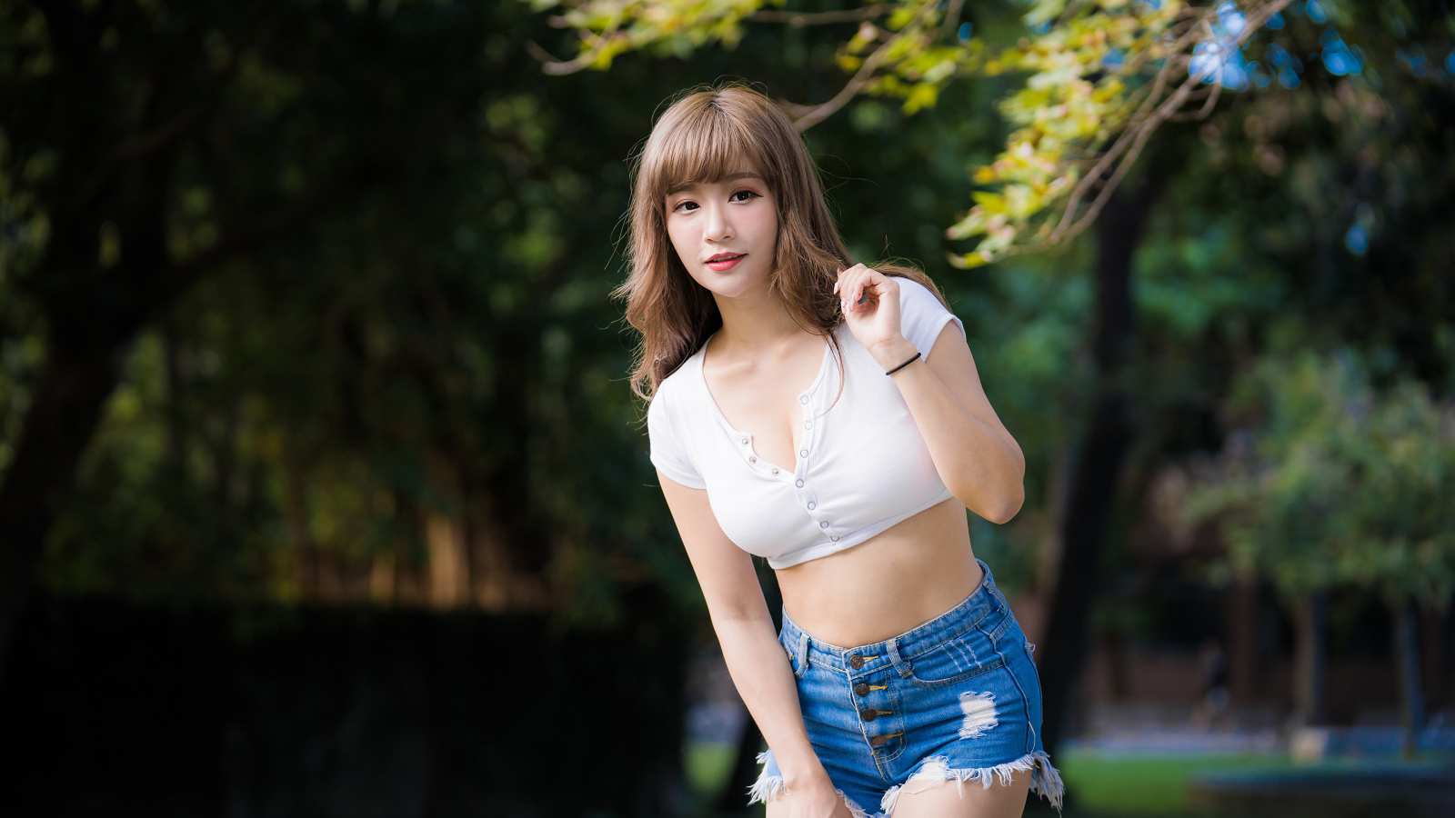 Молодая азиатка в белом топе и синих шортах  в парке