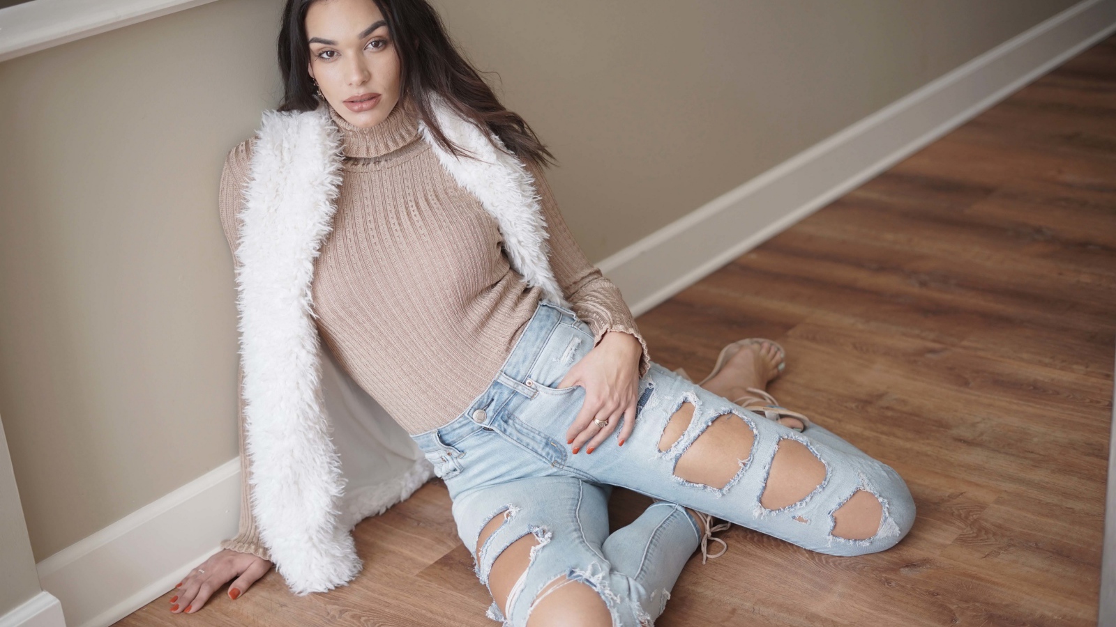 Молодая девушка в рваных джинсах сидит у стены