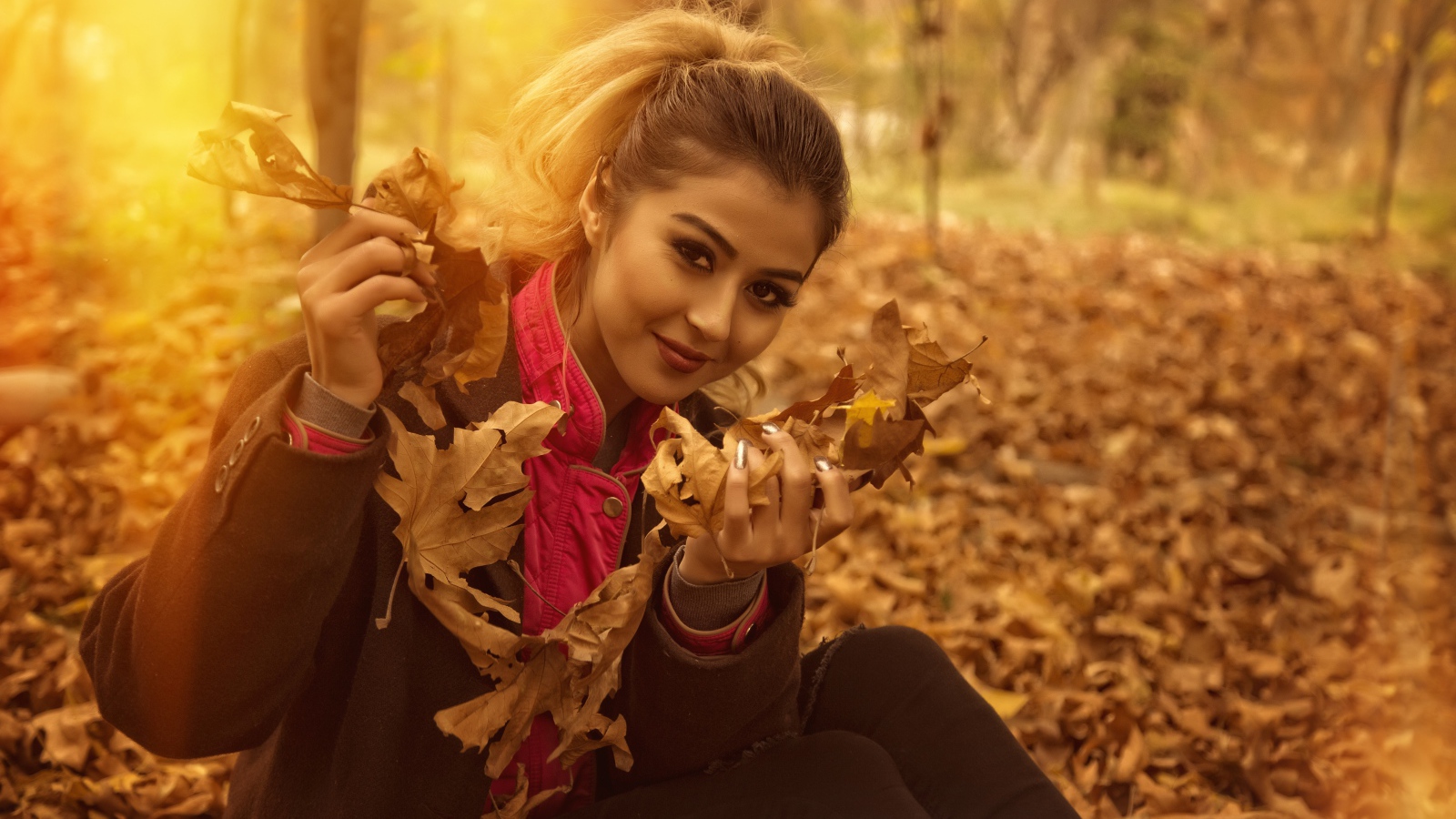 Молодая девушка с опавшими листьями в руках в парке