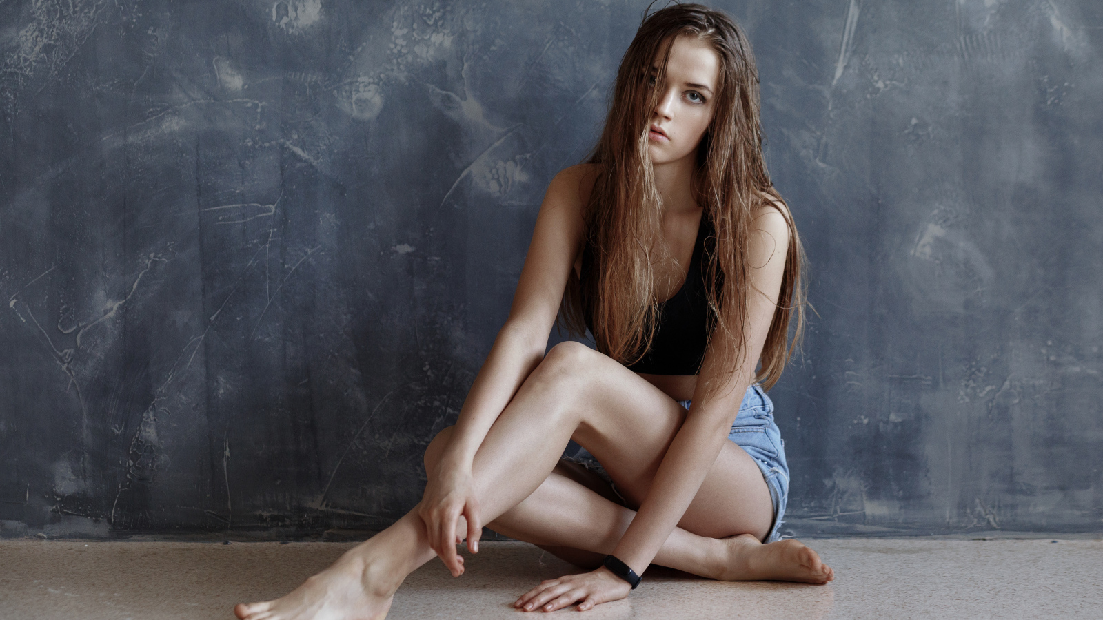 Молодая девушка с мокрыми волосами сидит у стены 