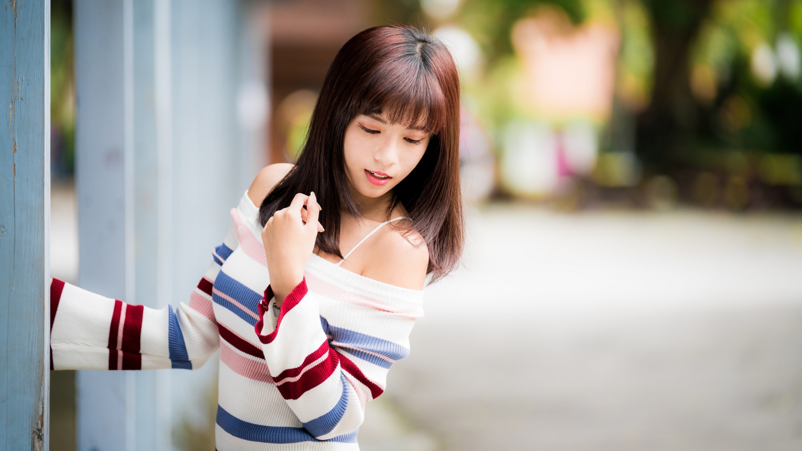 Молодая нежная девушка азиатка в свитере стоит у забора 