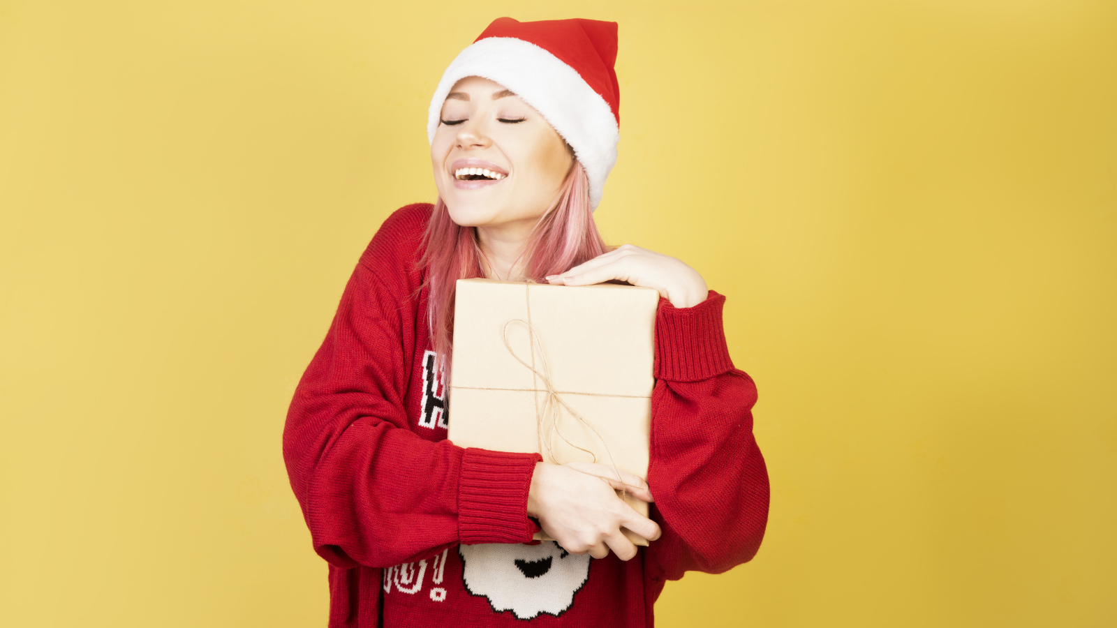 Улыбающаяся девушка в красном свитере с подарком на желтом фоне