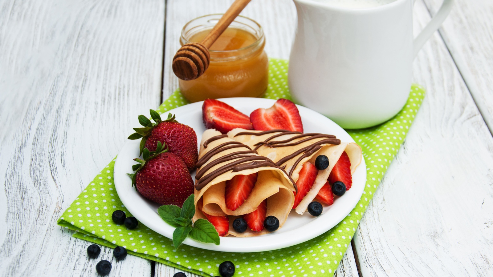 Вкусные блины с клубникой на столе с молоком и медом на праздник Масленица