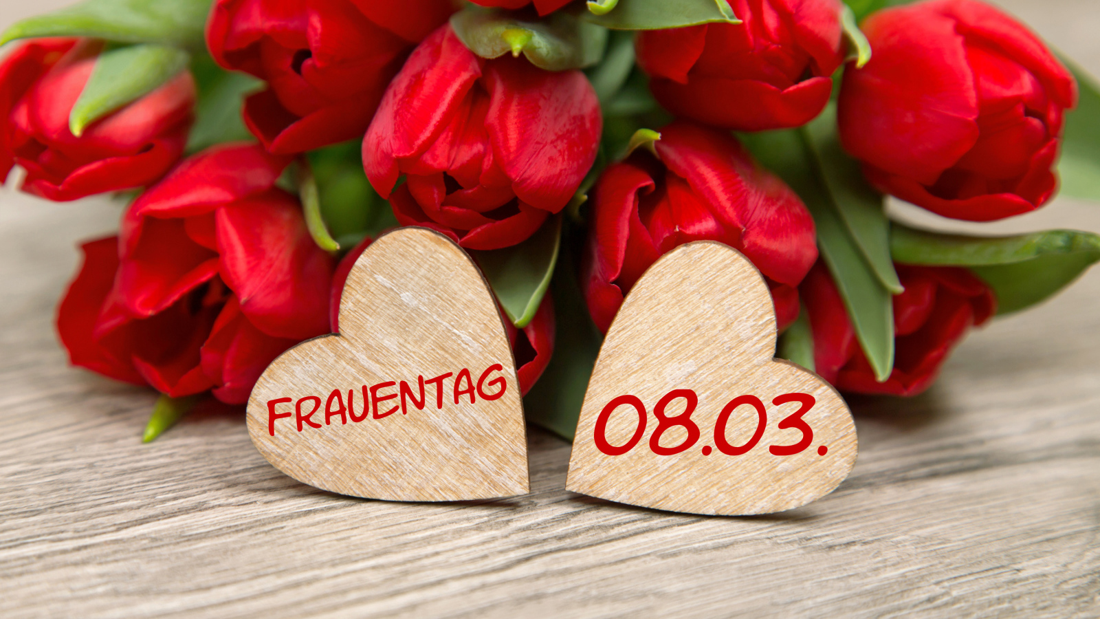 Два сердечка на столе с букетом красных тюльпанов на 8 марта 