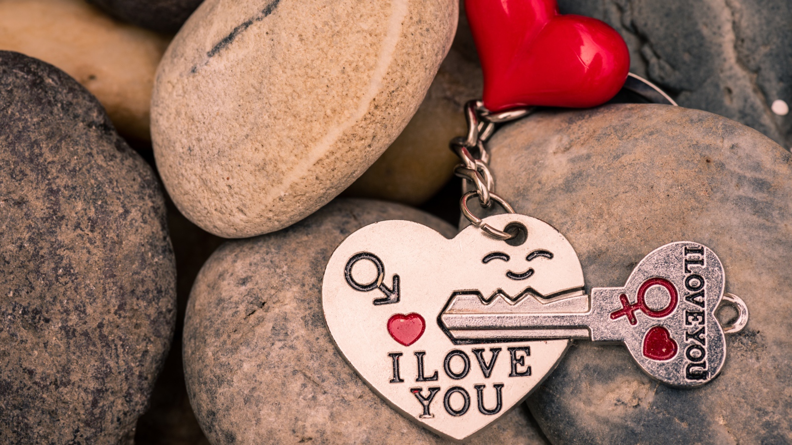 Брелок в форме сердца с ключом лежит на камнях 
