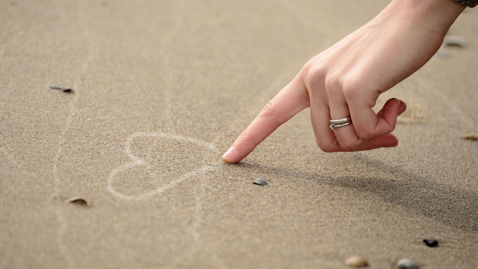 Девушка рисует сердце на песке 
