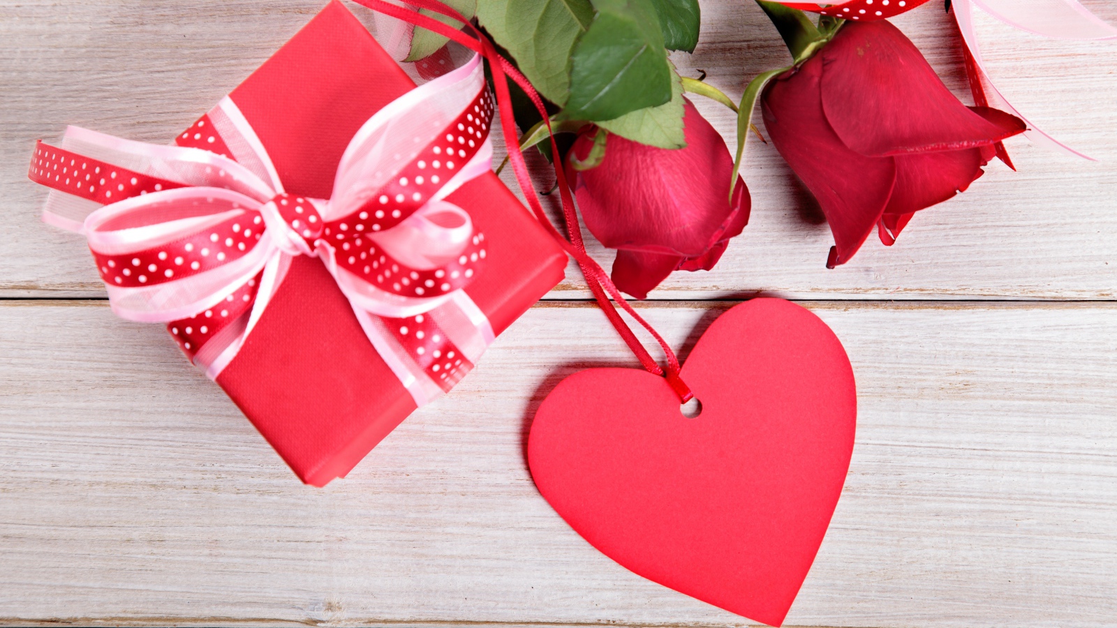 Красные розы с подарком и красным сердцем на деревянном столе