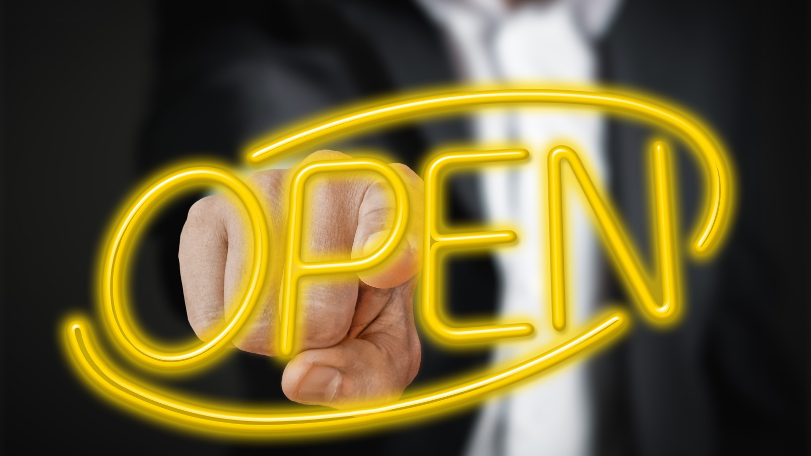 Мужчина трогает пальцем желтую  неоновую  надпись Open 