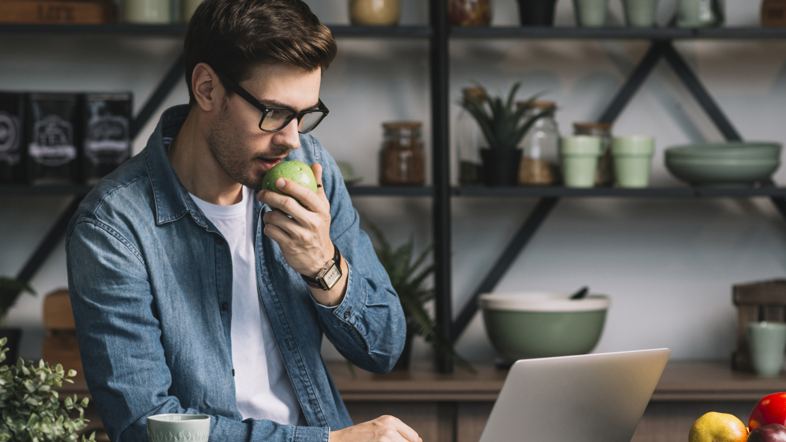 Мужчина с ноутбуком ест яблоко в кафе 