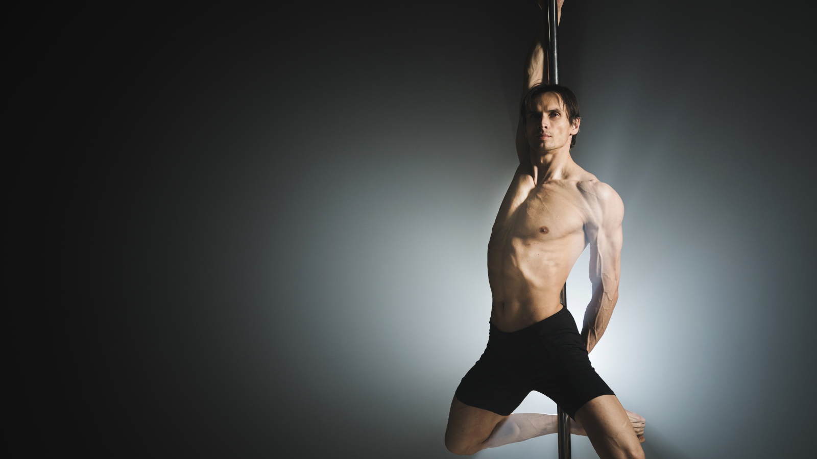 Мужчина танцует на пилоне на сером фоне