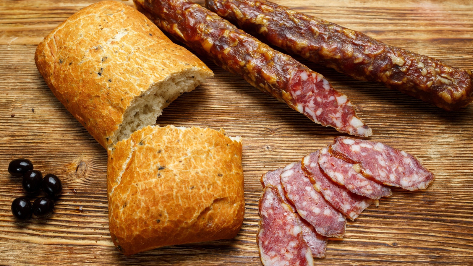 Сухая колбаса на столе с батоном и оливками