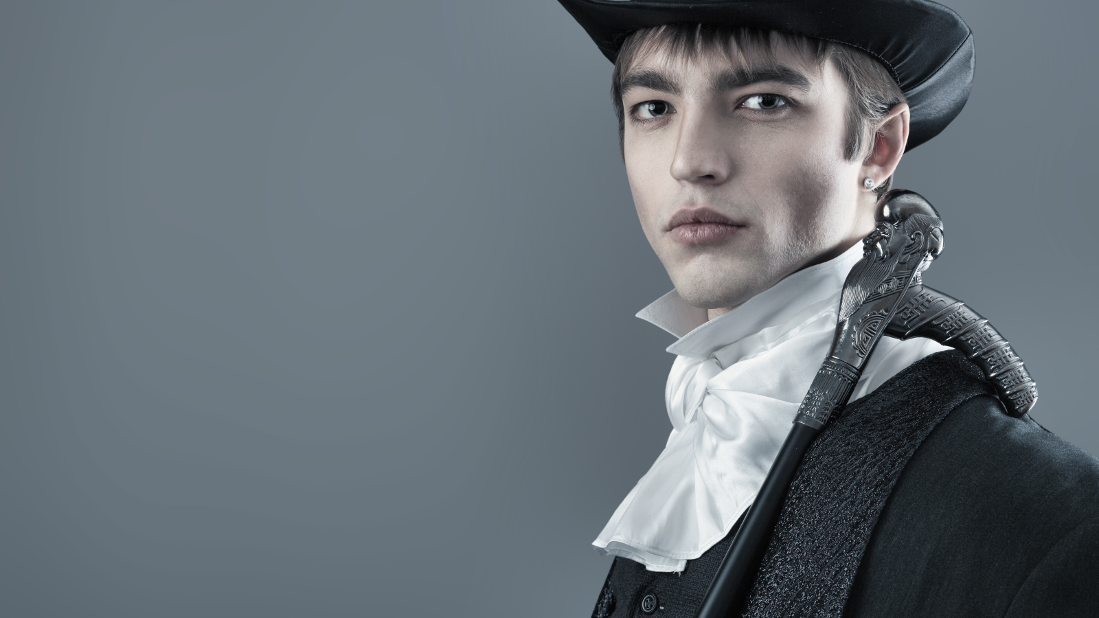 Красивый молодой человек в черном цилиндре и фраке на сером фоне