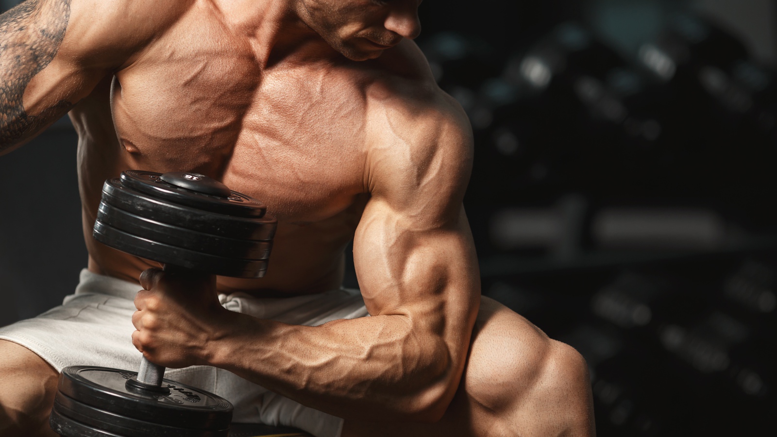 Сильный мужчина качает мускулы гантелей 