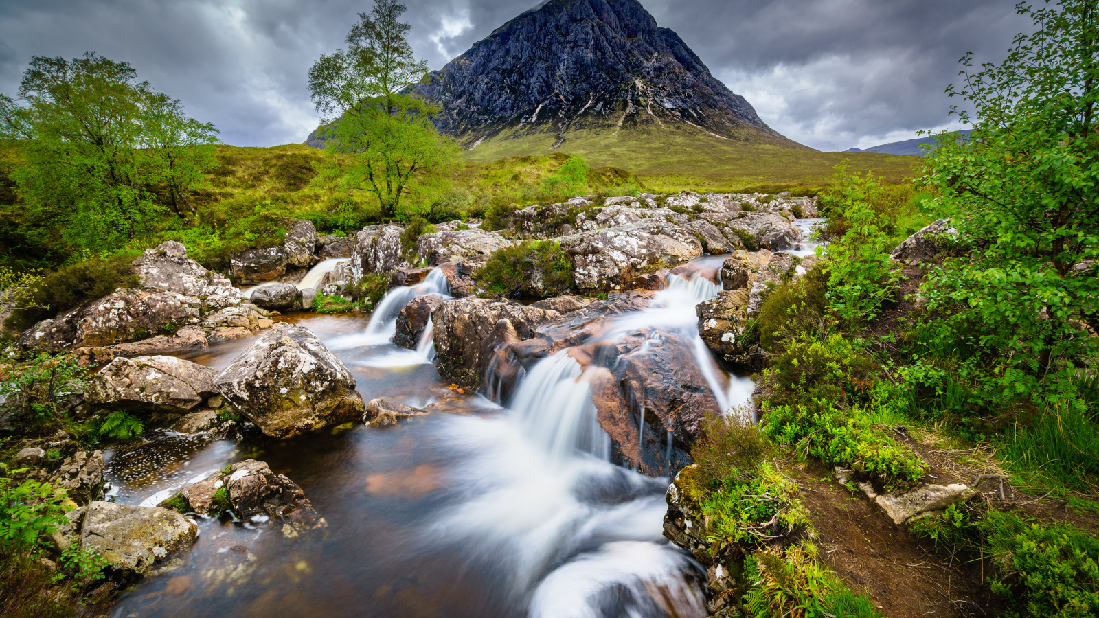 Быстрая вода в реке на фоне высокой горы под грозовым небом 