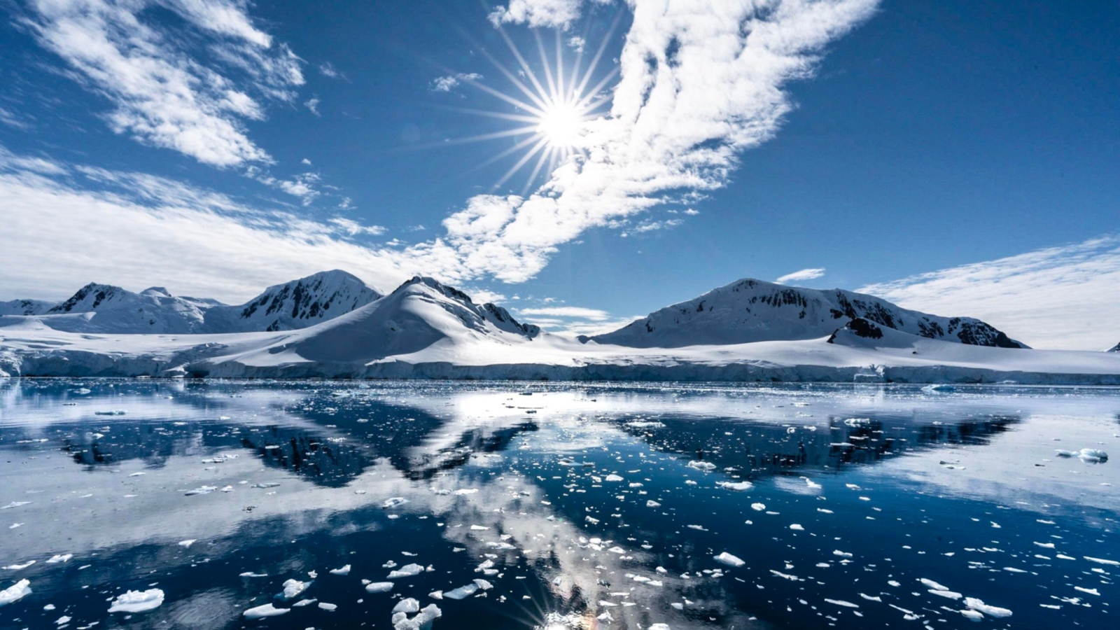 Белые облака в солнечном небе отражаются в озере у заснеженных гор 