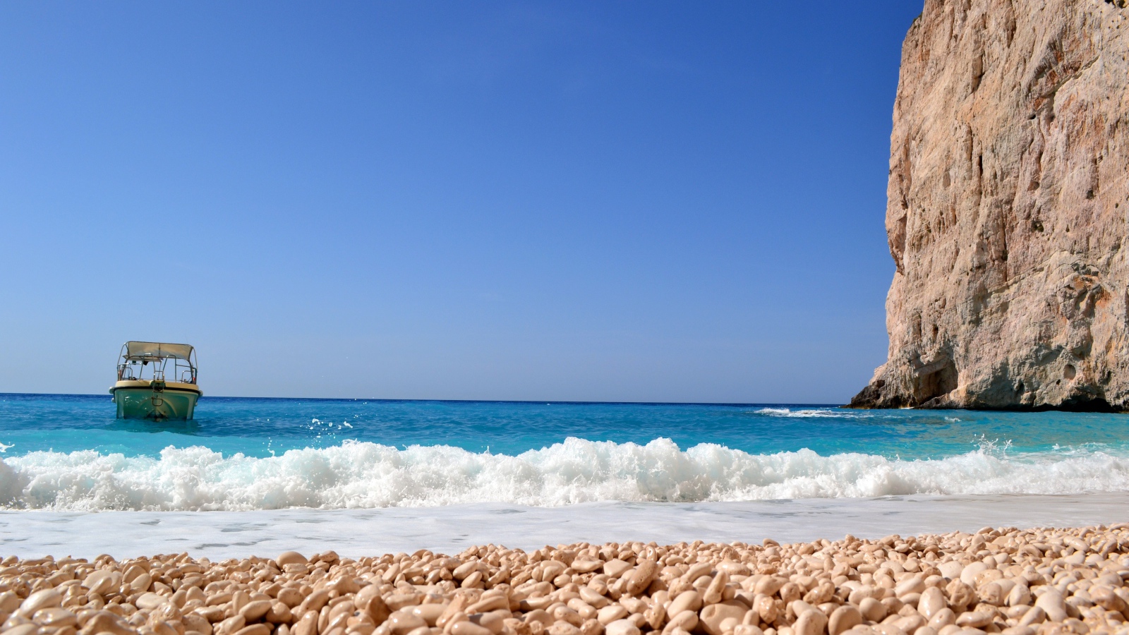 Красивая голубая вода с белыми волнами на пляже с галькой 
